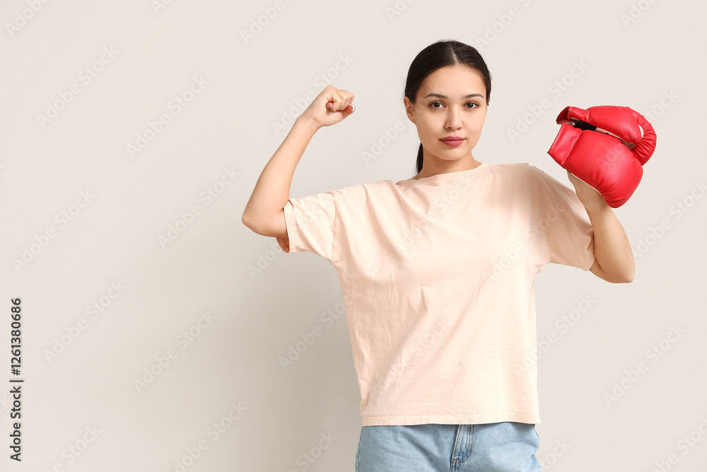 Naklejka premium Young woman with boxing gloves flexing muscles on white background. Feminism concept