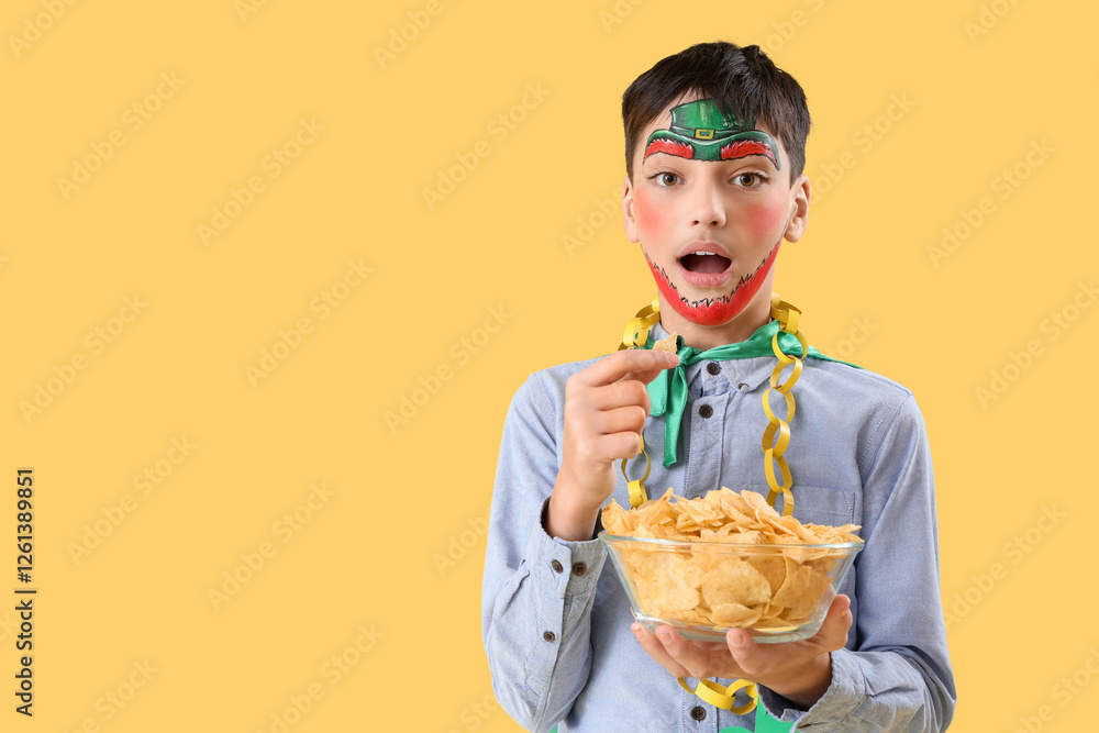 Surprised boy with face painting and potato chips on yellow background. St. Patrick's Day celebration Surprised boy with face painting and potato chips on yellow background. St. Patrick's Day celebration