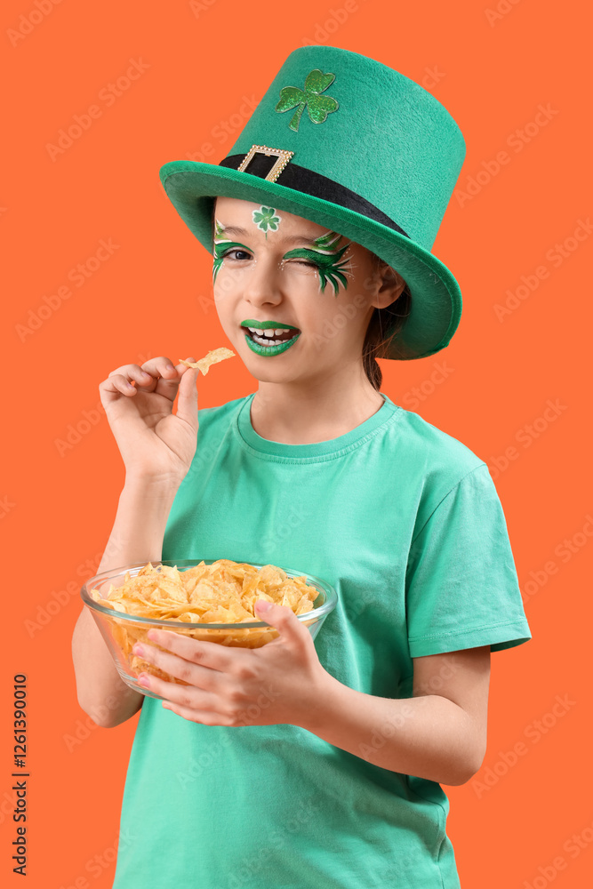Funny girl with face painting, leprechaun's hat and potato chips on orange background. St. Patrick's Day celebration Funny girl with face painting, leprechaun's hat and potato chips on orange background. St. Patrick's Day celebration