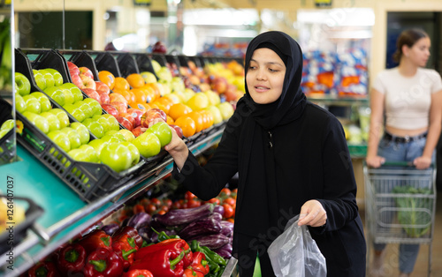 Asian girl in hijab buys ripe bell peppers in the supermarket photo