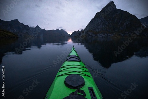 A sea kayak on a glassy lake at dusk and surrounded by mountains. 