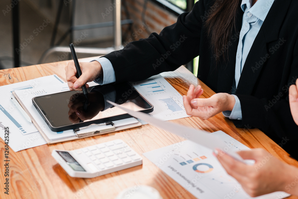 Business team working on financial analysis using a tablet and documents at a wooden desk in a modern office. Business team working on financial analysis using a tablet and documents at a wooden desk in a modern office.