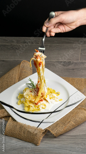 45-degree angle shot of a pasta dish, featuring a fork lifting pasta held by a hand. The creamy texture and vibrant colors enhance the appetizing contrast of sauce, cheese, and fresh herbs.