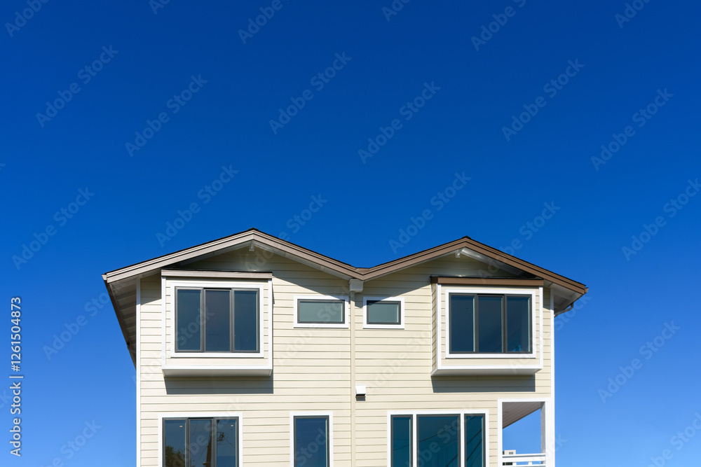 Exterior view of upper floors of contemporary residential building with beige siding, large windows, and a symmetrical design, set against a vibrant, clear blue sky Exterior view of upper floors of contemporary residential building with beige siding, large windows, and a symmetrical design, set against a vibrant, clear blue sky