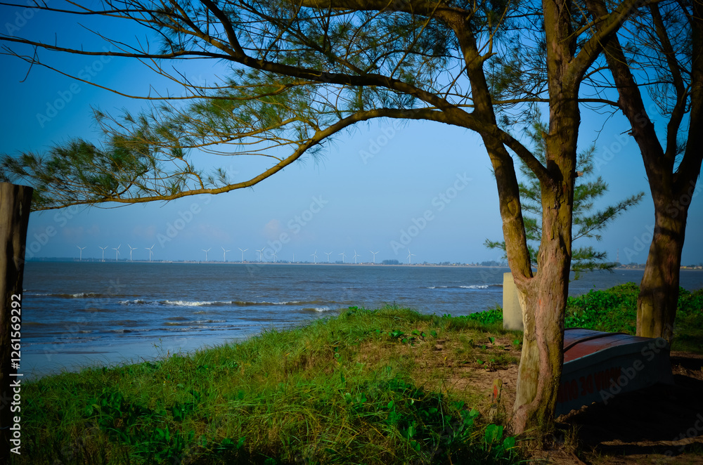 A serene coastal scene with trees in the foreground and wind turbines in the distance. A serene coastal scene with trees in the foreground and wind turbines in the distance.