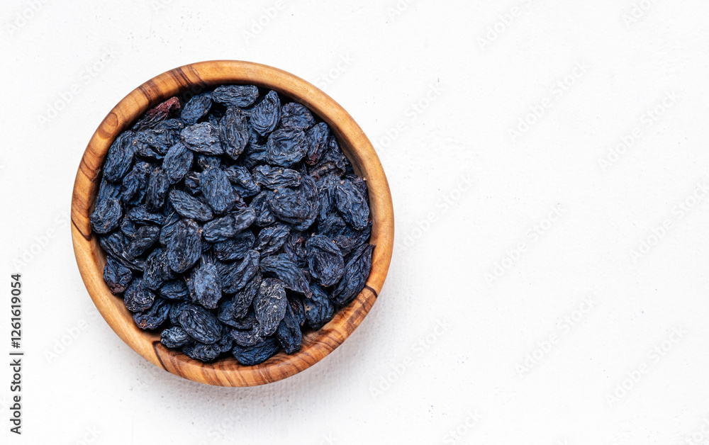 Φωτογραφία Organic sun dried black blue raisins in wooden bowl on white background, top vie