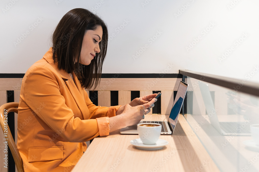 Young woman is working remotely from a coffee shop, using phone and working on her laptop Young woman is working remotely from a coffee shop, using phone and working on her laptop