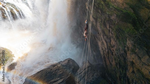 Tablou pe pânză Woman abseiling upside down in front of a waterfall in Minas Gerais