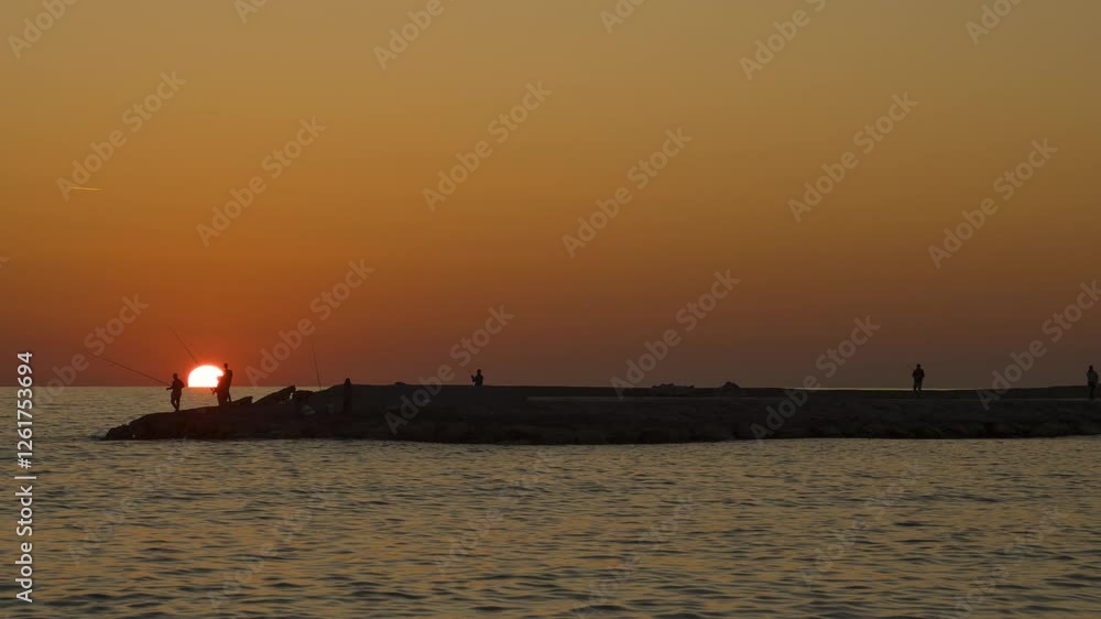 Time Lapse of Fishermen Casting Fishing Rods on a Rocky Pier at Sunset over the Sea with an Orange Sky in Silhouette Time Lapse of Fishermen Casting Fishing Rods on a Rocky Pier at Sunset over the Sea with an Orange Sky in Silhouette