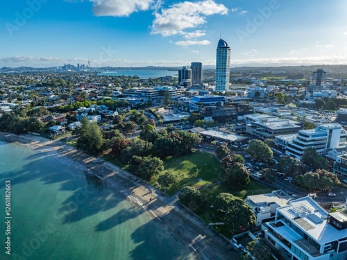 High-angle view of Auckland, New Zealand, showcasing the city's urban sprawl, a beach, and parkland. People relax on the beach and in the park. TAKAPUNA, AUCKLAND, NZ