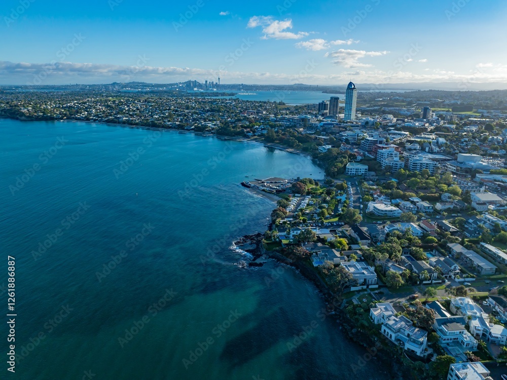 Fototapeta premium Aerial view of Auckland, New Zealand, showcasing coastal residential areas and the city skyline. Coastal homes and city buildings are visible. TAKAPUNA, AUCKLAND, NZ