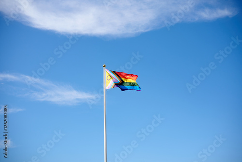 Progress pride flag waving on flagpole with blue sky background