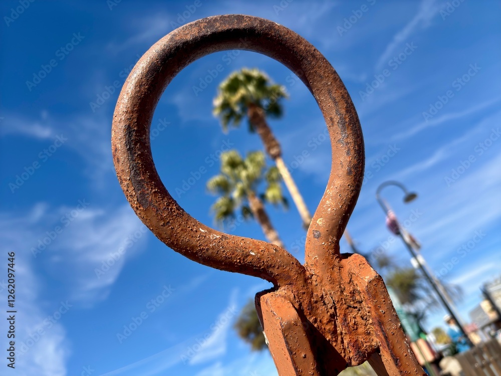 Rusty metal loop in focus with blurred palm trees and blue sky behind Rusty metal loop in focus with blurred palm trees and blue sky behind