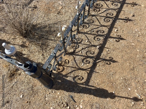 Ornate wrought iron fence casting shadows on dry ground. photo