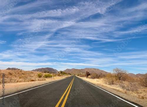 Desert highway leading to distant Arizona mountains under blue sky
