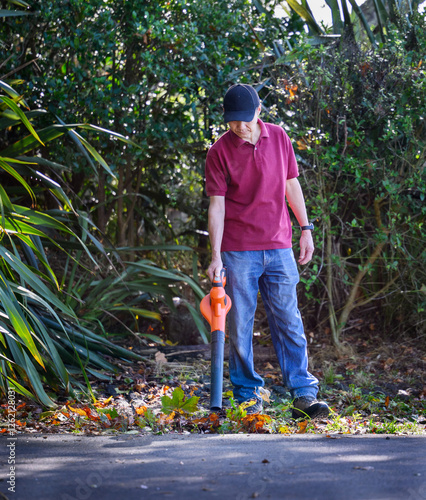 Obraz na płótnie Man cleaning fallen autumn leaves using a leaf blower along the driveway. w salonie