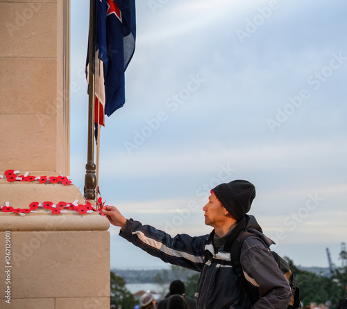 Man placing red poppies on the wall. Anzac Day commemoration. Auckland. Vertical format.