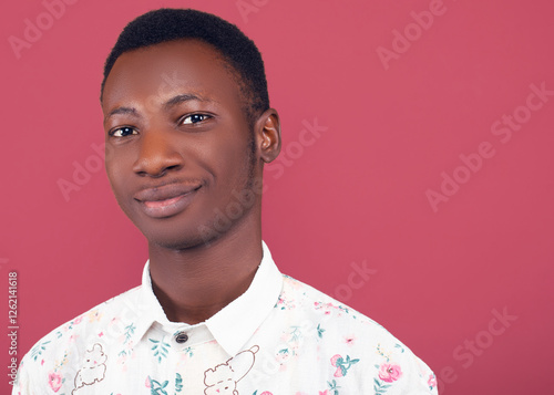 Close-up headshot of a young man with short black hair, smiling warmly while wearing a floral shirt. The coral background and studio lighting enhance his friendly and approachable expression.