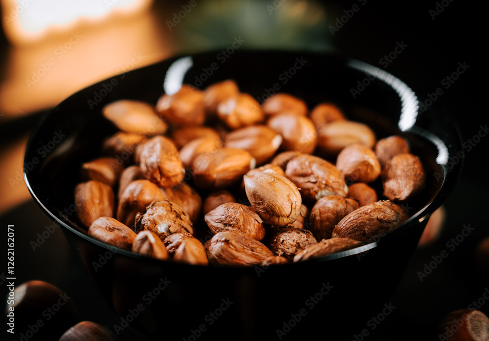 Freshly roasted hazelnuts in a black plate showcasing natural texture and color against a dark background