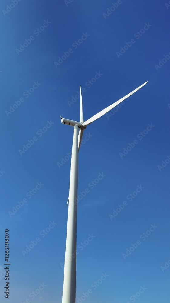 A towering wind turbine against a clear blue sky represents renewable energy and sustainability. Harnessing wind power, this eco-friendly technology drives a cleaner, greener future. Vertical 4k video A towering wind turbine against a clear blue sky represents renewable energy and sustainability. Harnessing wind power, this eco-friendly technology drives a cleaner, greener future. Vertical 4k video