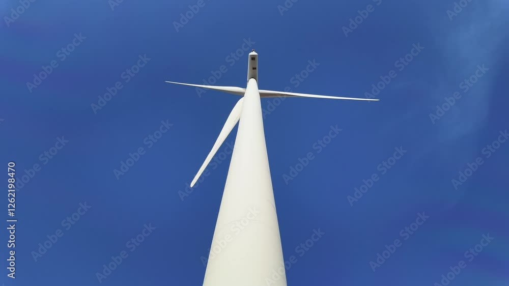Low-angle view of a wind turbine against a vibrant blue sky, symbolizing renewable energy, sustainability, clean power. Wind energy drives the future of eco-friendly electricity generation. 4k video Low-angle view of a wind turbine against a vibrant blue sky, symbolizing renewable energy, sustainability, clean power. Wind energy drives the future of eco-friendly electricity generation. 4k video