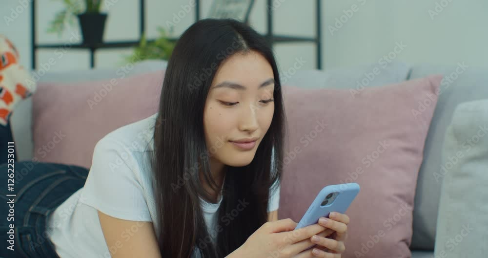 Beautiful and happy, young woman lying on the sofa. Interact with phone application, scroll and text on screen. Use social media or online shopping. Beautiful and happy, young woman lying on the sofa. Interact with phone application, scroll and text on screen. Use social media or online shopping.