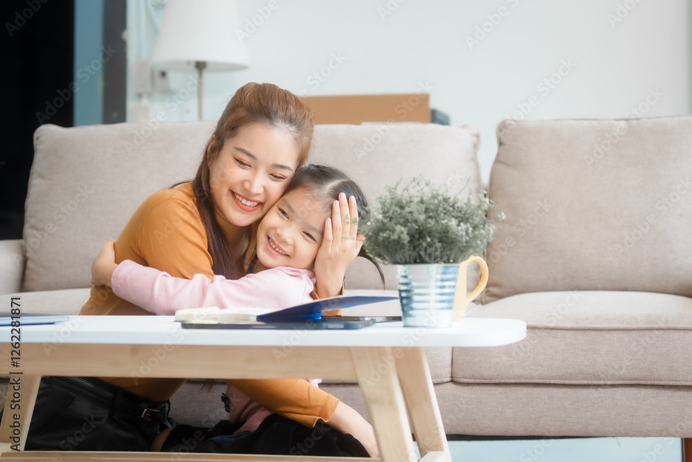 Asian young mother and her daughter sit together on the sofa in the cozy living room, working on homework at the desk, creating a warm and supportive atmosphere for learning, love, hug, mother days. Asian young mother and her daughter sit together on the sofa in the cozy living room, working on homework at the desk, creating a warm and supportive atmosphere for learning, love, hug, mother days.