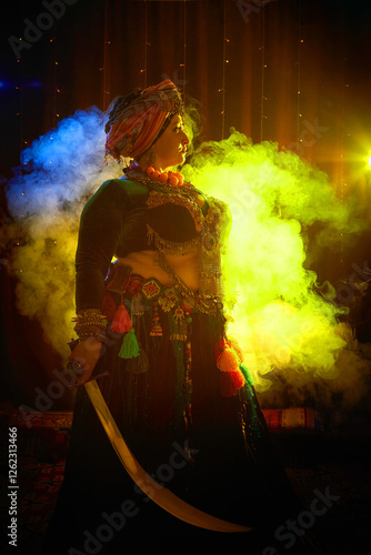 A woman in a colorful headscarf and jewelry poses With a saber in front of a wall of colorful tassels and smoke around photo