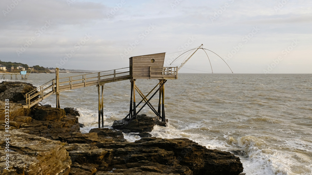 Traditional French fishing hut on stilts with carrelet net over ocean. Wooden structure stands on rocky shore, with waves and cloudy sky. Ideal for projects to travel, culture, or traditional fishing. Traditional French fishing hut on stilts with carrelet net over ocean. Wooden structure stands on rocky shore, with waves and cloudy sky. Ideal for projects to travel, culture, or traditional fishing.