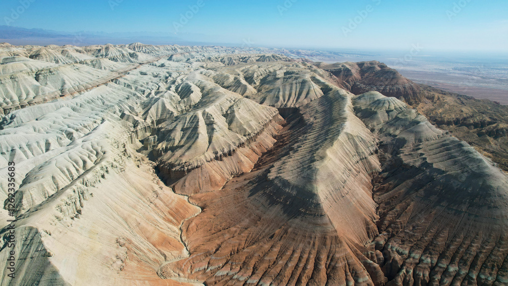Aerial view of the colorful aktau mountains under a clear blue sky, showcasing the unique geological formations and vastness of the landscape in kazakhstan