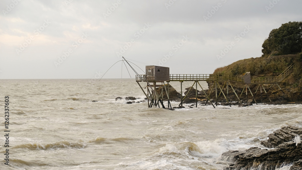 Traditional French fishing hut on stilts with carrelet net over ocean. Wooden structure stands on rocky shore, with waves and cloudy sky. Ideal for projects to travel, culture, or traditional fishing. Traditional French fishing hut on stilts with carrelet net over ocean. Wooden structure stands on rocky shore, with waves and cloudy sky. Ideal for projects to travel, culture, or traditional fishing.