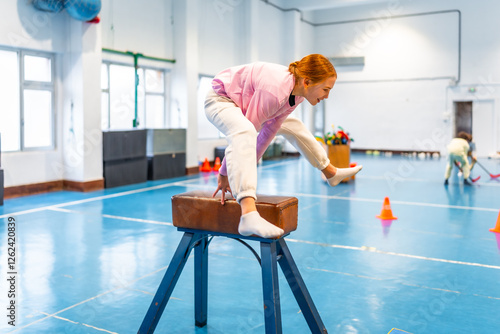 Slika na platnu Young girl balancing on pommel horse during gymnastics class at school gym