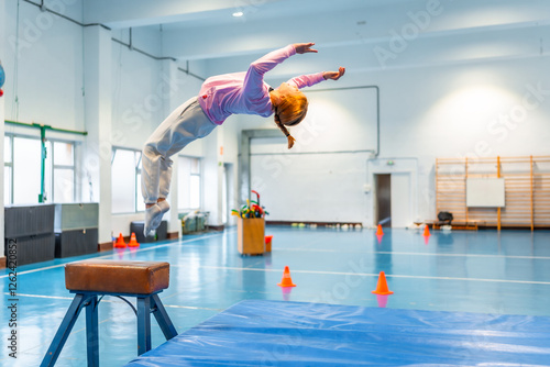Fotografie Young gymnast performing backflip over vault in school gym class