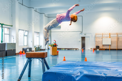 Obraz na plátně Young gymnast performing a backflip over vaulting horse in school gym