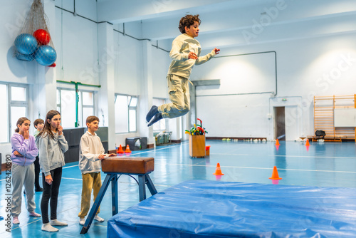 Canvas Print Teenage boy performing gymnastics jump in school gym class with classmates watch