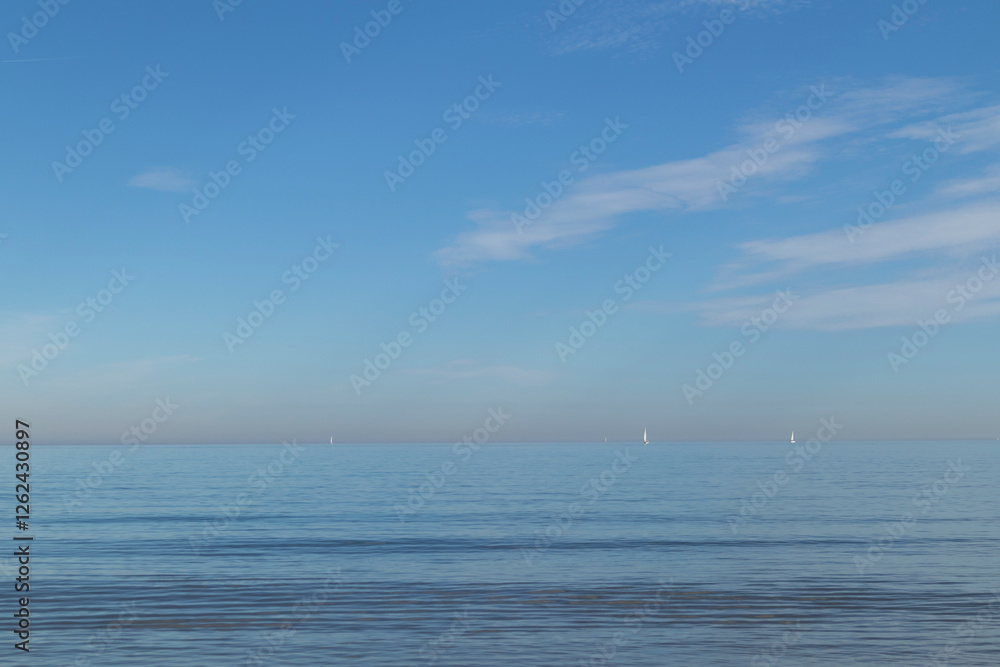 Calm sea with blue sky and sailboats on the horizon Calm sea with blue sky and sailboats on the horizon