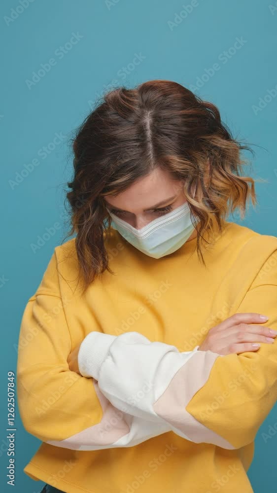 Vertical screen sad young woman in medical mask on blue background puts her hands down lowers her head with regret sadness in her eyes. lockdown quarantine covid 19 pandemic virus panic lifestyle Vertical screen sad young woman in medical mask on blue background puts her hands down lowers her head with regret sadness in her eyes. lockdown quarantine covid 19 pandemic virus panic lifestyle
