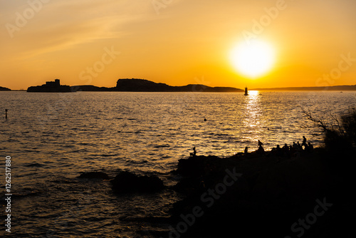 Coucher de soleil sur un paysage marin à Marseille, une île en arrière plan et ligne d'horizon avec dix personnes assises sur des rochers en premier plan photo