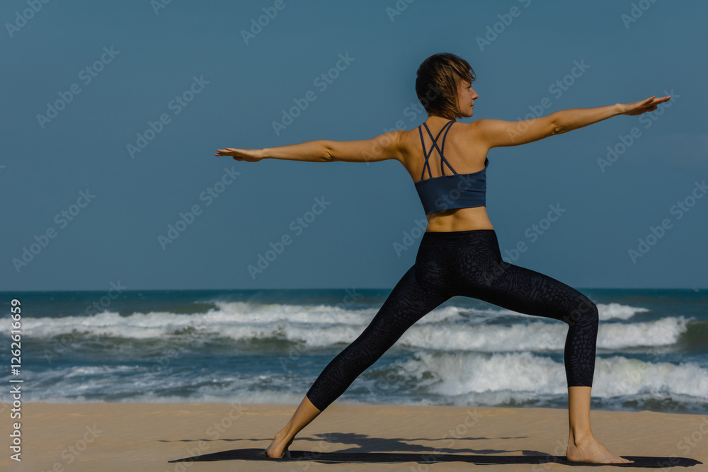 Female adult practicing yoga on beach with ocean waves under blue sky Female adult practicing yoga on beach with ocean waves under blue sky