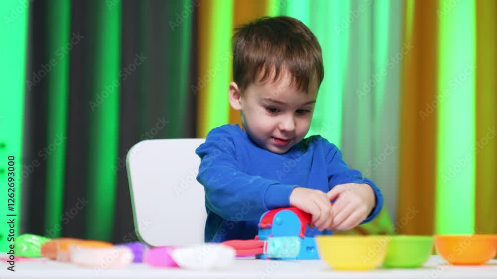 Cute smiling baby boy presses the mold machine. Lovely toddler opens the device and winks at the result plasticine. Cute smiling baby boy presses the mold machine. Lovely toddler opens the device and winks at the result plasticine.
