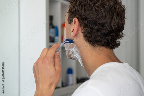 Obraz na płótnie A detailed view of a man using a disposable razor to shave his beard in a bathroom setting. w salonie