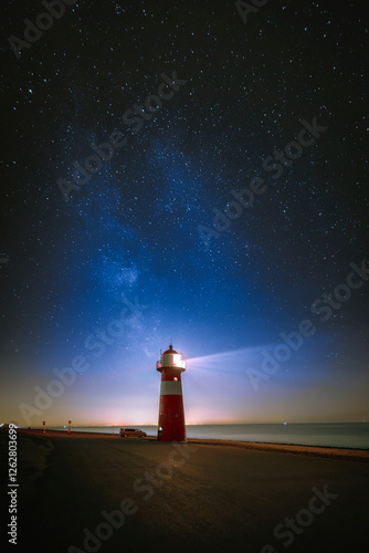 The Milky Way photographed at night with stars in the sky above a light beacon on the shor