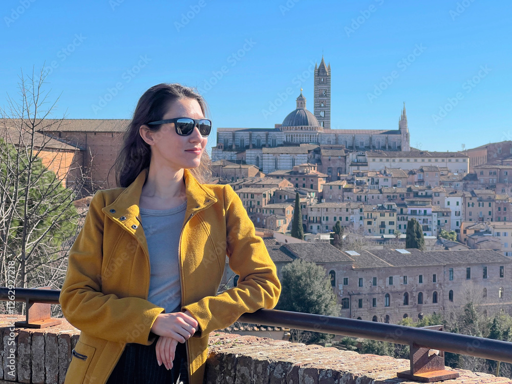 Fototapeta premium A portrait of a young woman at the background Siena historical city center panorama. Self tourism concept. Travel in Italy in winter