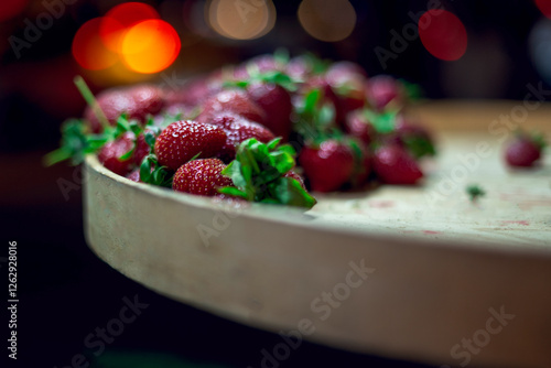 Organic strawberries on a wooden slate with bokeh lights in an outdoor market stall, close up