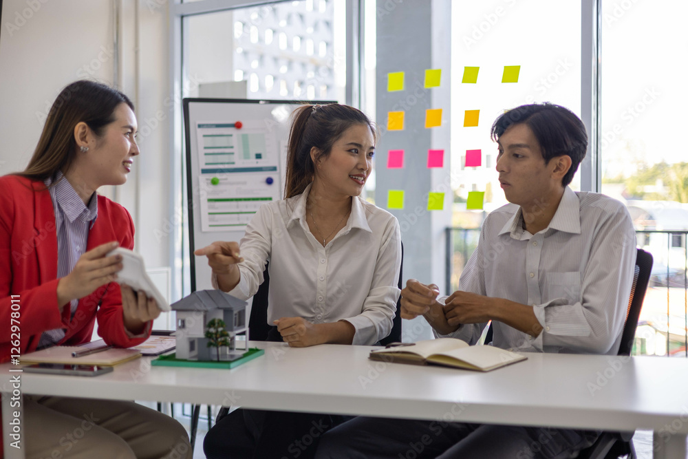 Three people are sitting at a table in a room with a whiteboard behind them. They are discussing something important
