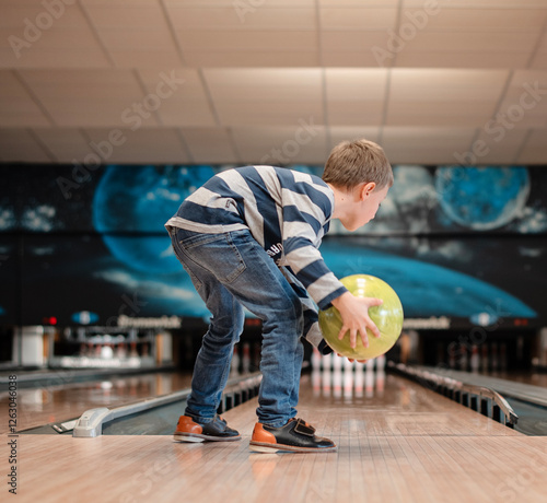 Playing bowling in sports centre. Bowler is going to throw bowling ball on the track and knock down pins. Selective focus. Boy plays bowling.