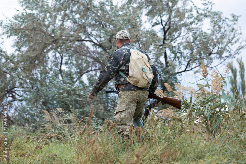 Mature hunter man holding a shotgun and walking through a field Mature hunter man holding a shotgun and walking through a field
