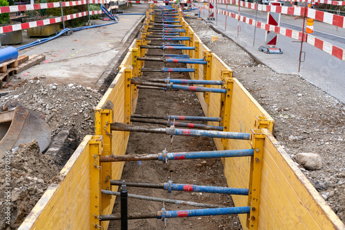 Trench on the road for renewal of urban infrastructure, like sewer system, cabling and fiber optics. Red white barriers all around the construction site.