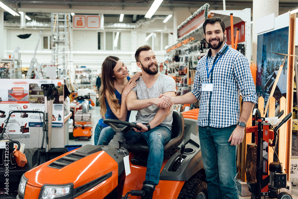 Salesman is showing couple of clients new cleaning machine in power tools store. Two men shaking hands. Salesman is showing couple of clients new cleaning machine in power tools store. Two men shaking hands.