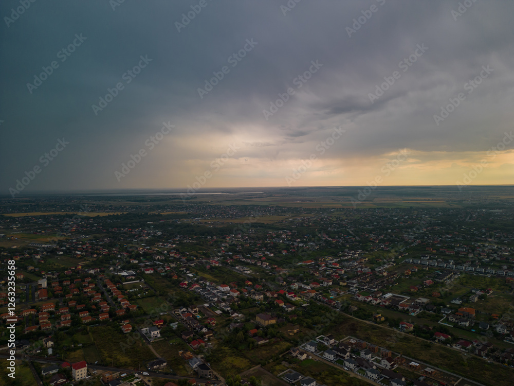 Fototapeta premium Rural settlement on the plain filmed from drone in cloudy summer weather. Beginning of a strong storm accompanied by thunder and lightning
